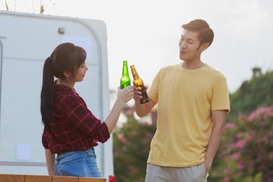 travel asian couple having fun drinking beers standing in front of vintage camper mini van. happy people enjoying drink and camping by the nature. concept of leisure vacation lifestyle.
