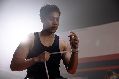 male boxer wraps a wrist band, asian man prepares to practice boxing at the gym.