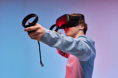 male boy wears vr glasses, has fun and entertains himself, plays video games using controllers, isolated in studio. teen experiences virtual reality, wears 3d glasses indoor. focus on hands