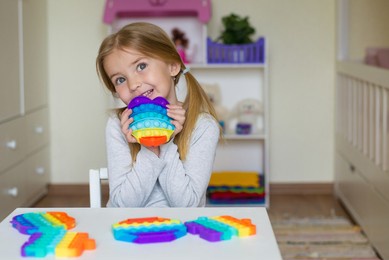 baby girl playing with rainbow pop it fidget. the push bubble fidget touch toy is a washable and reusable silicone toy. anti-stress toy for an autistic child. the concept of mental health popit toy