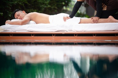 asian man enjoy a massage by the resort's pool. 