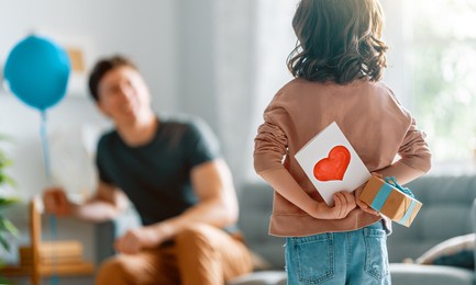 child daughter is congratulating her father and giving him postcard. dad and girl are smiling. family holiday and togetherness.