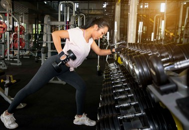 young asian women training do muscle building exercises using dumbbells.young fitness woman taking a dumbbell from rack in  gym.fitness dumbbells, weights equipment,gym sport fitness concept.
