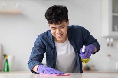 cheerful asian guy cleaning kitchen table with spray and dust cloth, happy with his job, closeup, copy space. smiling young chinese man house-keeping after moving to new apartment