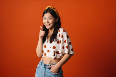 smiling young asian woman in summer clothes standing over orange background