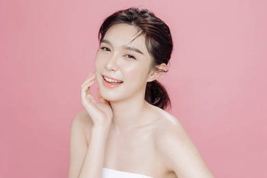 asian woman has a lovely face is feeling happy with her perfect skin touch her face. she wears a white strapless bra. isolated over pink background. skincare, cosmetology and plastic surgery concept.