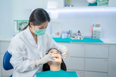 asian young dentist wearing face mask, using medical instruments for oral care check up. doctor examining for cavities and gum disease. medical occupation service and health care in dental clinic.