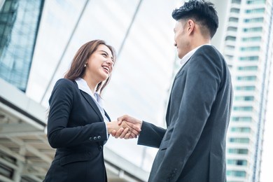 asian businessman and woman handshake in the city with highrise building in background. partnership agreement successful after complete the negotiation. business deal, merger and acquisition concepts.