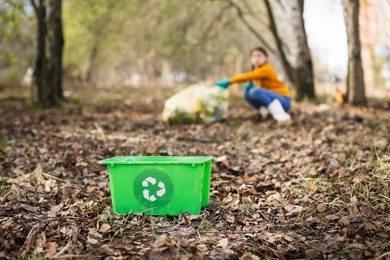 green container for recycling, against the background of children collecting garbage in the park, in the forest. caring for the environment, education of environmental friendliness in children