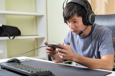 happy young asian esport gamer man is playing skills game on smartphone game, feels fun, excited at home. playing game is relaxing and resting after working or studying as hobby. playing game concept.
