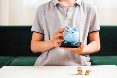 teen boy holding blue piggy bank. kids financial education and responsibility, accumulation and savings planning. the child manages and deposits his finance, investment concept.