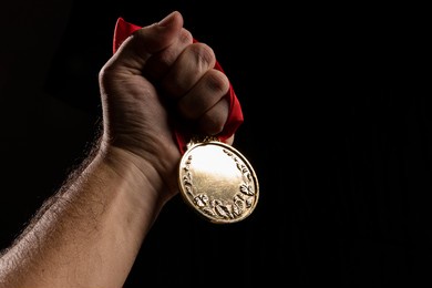 hand holding a gold medal on black with blank face for text, concept for winning or success