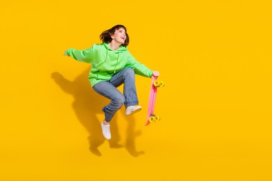 full length body size view of pretty cheery girl jumping riding skate having fun spare time isolated over bright yellow color background