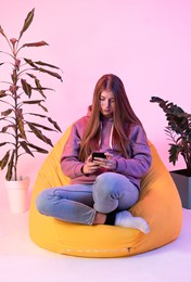 the girl flips through the instagram page. he looks at the phone and sits in a chair.