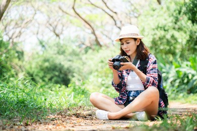 beautiful asian woman using a camera in forest during the summer. travel activities trekking during the holidays.