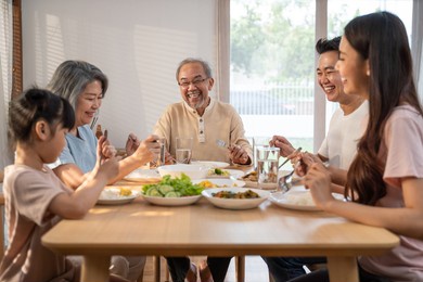 big asian happy family spend time having lunch on dinner table together. little kid daughter enjoy eating food with father, mother and grandparents. multi-generation relationship and activity in house