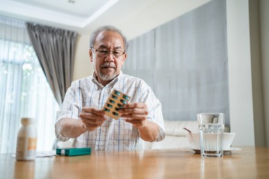 asian senior elderly male patient on eating table at nursing home care. older man wearing eyeglasses and look to medicine pill in blister pack, read prescription and content. medical insurance concept