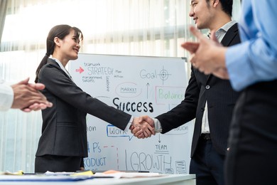 asian businessman and woman handshake after negotiations for business deal, merger and acquisition in meeting room. employee worker team clap hand and enjoy partnership agreement to success in company