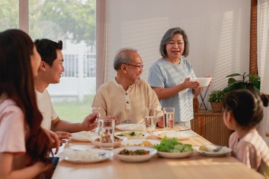 asian extended family having breakfast together at home. asian big family grandparents parents and kid enjoy eating and talking with happy moment.