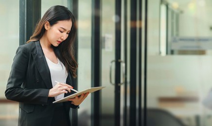 beautiful businesswoman using stylus pen writing on tablet screen while standing in office room with copy space.