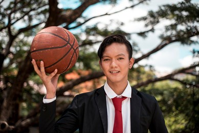 a young college varsity student holding an old basketball while at the park