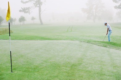 golfer chipping onto the green at sunrise on the golf course in misty conditions