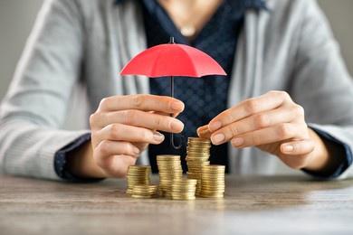 young woman hands holding red umbrella over stacked coin on table. female hand holding a small umbrella to protect heaps of coins while saving them. financial security and savings protection concept.