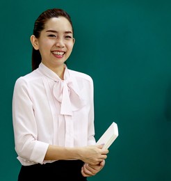 portrait shot of asian young beautiful female professor teacher lecturer standing holding text book in hands look at camera while teaching lesson to elementary school children students in classroom.