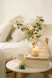 still life details in home interior of living room. book, hot cup tea, candle and vase with apple spring flowers. read and rest. cozy spring concept.