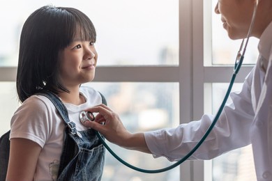 pediatric care with happy child patient and pediatrician doctor examining asian girl kid heart and lung health with stethoscope in medical clinic, healthcare checkup service concept
