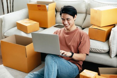 asian business men sit on sofa use laptop computer checking customer order online shipping boxes at home. starting small business entrepreneur sme freelance. online business, work at home concept.