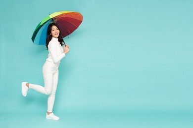 young asian woman holding rainbow umbella standing isolated on green background, full body