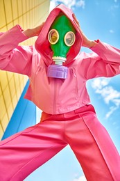 technological disaster concept, air pollution. portrait of a woman in bright pink clothes and a green gas mask against a blue sky and yellow industrial wall.