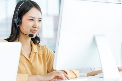 focus asian beautiful attractive female call center cheerful happily smiling with headsets, sitting,  monitoring in office or agency at computer screen, giving service to customers