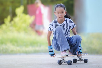 selective focus, young asian girl surfing or skating at the park in the morning. play sports safely concept.