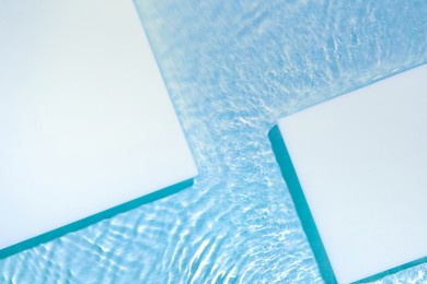 two empty white square podium on transparent clear calm blue water texture with splashes and waves in sunlight abstract nature background for product presentation flat lay cosmetic mockup, copy space.