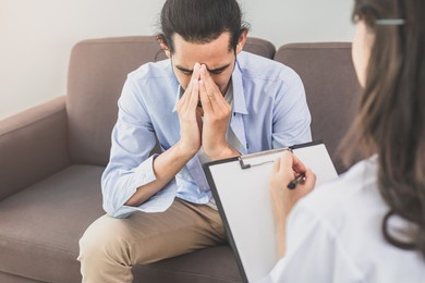 asian young man, male has mental symptoms which must have been therapy and stress, sitting on couch to consult to psychologist during the session  taking notes to find out how to treat the therapist.