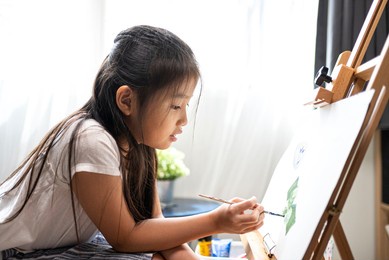 asian beautiful girl with brush nd palette painting water color to canvas on wooden easel at home for her relaxing time.