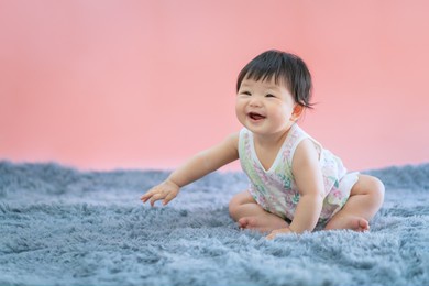 asian baby smiling and sitting on carpet with pink color background. cute 6 months baby sitting with copy space use as concept of valentine, love, learn, education, baby or kid department in hospital.