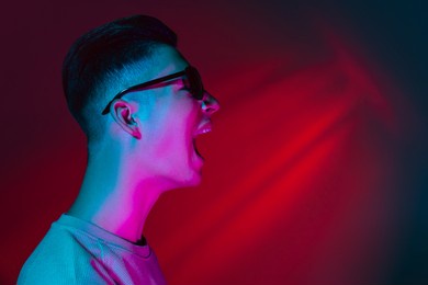 shout with joy. young man isolated on dark red background in neon pink light. handsome male model in casual style. concept of emotions, facial expression, youth. copy space for ad.