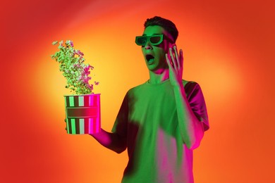 movie, cinema. excited happy young man with popcorn isolated on orange background in neon pink light. handsome male model in casual style. concept of emotions, facial expression. copy space for ad.