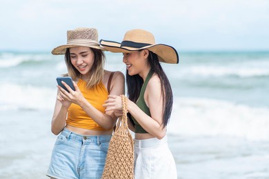two asian girl friends wearing hats for a walk on the beach using their smartphones to checkin beach locations on social networks 
