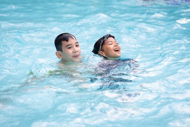 asian girl and boy playing water and swimming together in the swimming pool with fun. summer activity and childhood lifestyle concept.