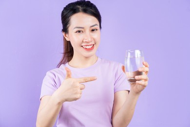 young asian woman holding glass of water on purple background