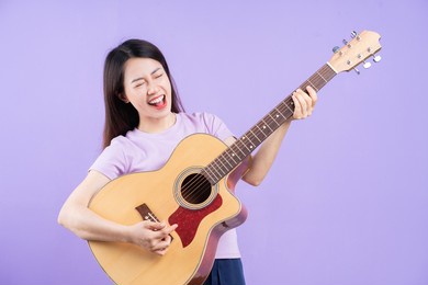 young asian woman playing guitar on purple background