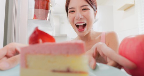 asian woman takes cake from opened refrigerator in kitchen at home happily