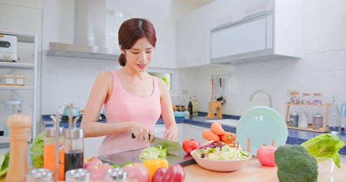 healthy asian woman making a salad in light white interior style kitchen at home