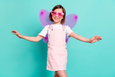 photo of adorable cute school girl wear pink overall glasses wings smiling dancing isolated teal color background