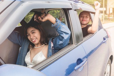 3 excited girlfriends together inside a small car, enjoying a road trip.