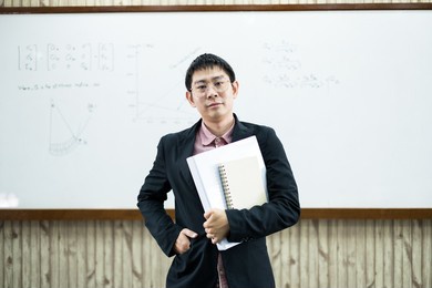 an asian male teacher in a classroom near the whiteboard is writing and teaching a lesson with a special lecture in a class column. math teacher explains arithmetic sums to university students.